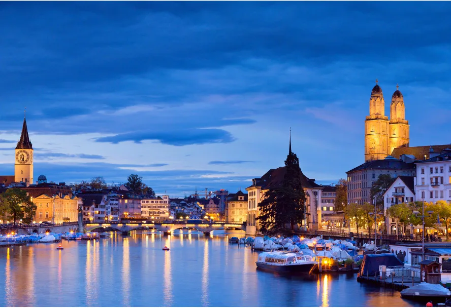Die Limmat zur blauen Stunde mit den Doppeltürmen des Grossmünsters und beleuchteten Booten
