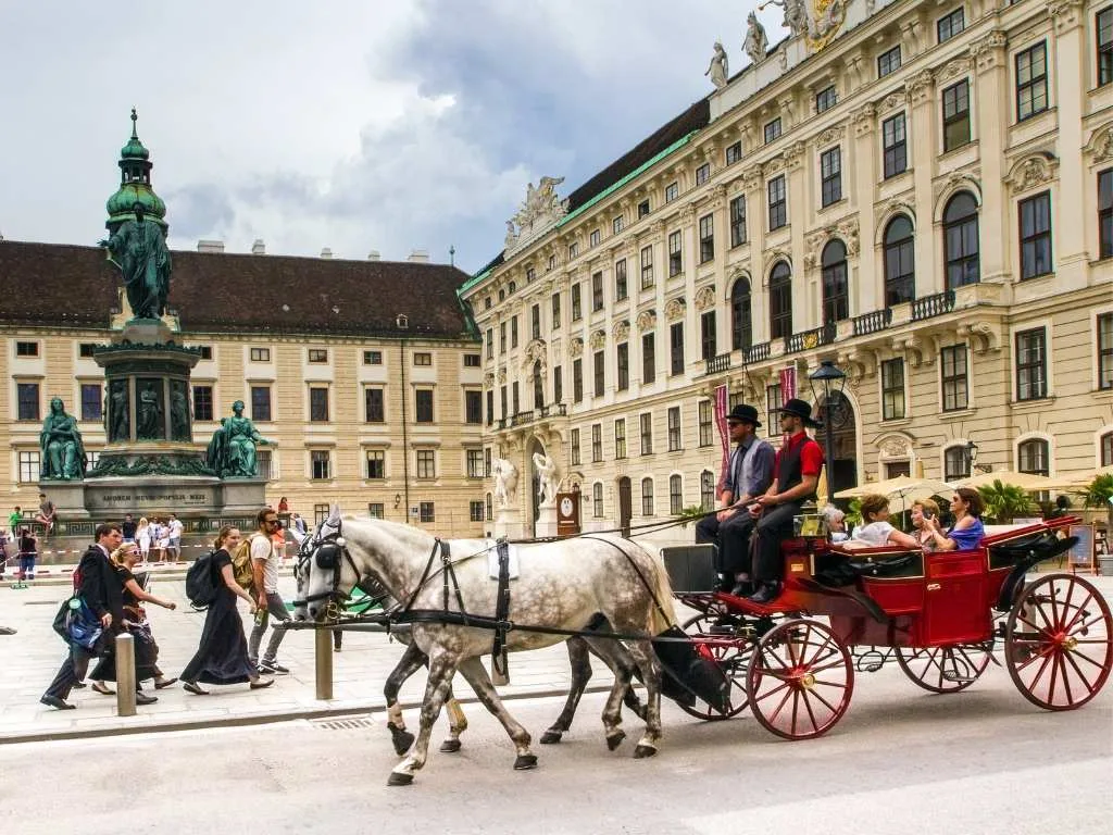 Ein Fiaker fährt durch den Innenhof der Hofburg an der barocken Fassade vorbei