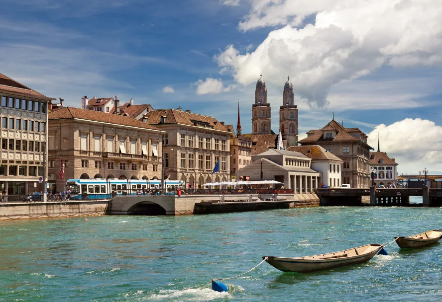 Der Limmatquai mit dem Grossmünster, davor ein blaues Tram und Boote auf dem Wasser