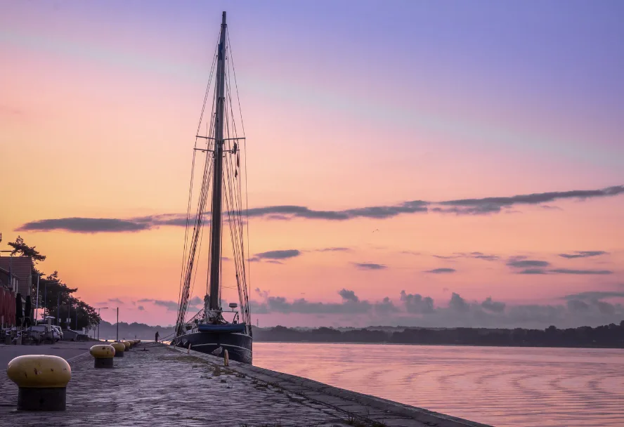 A single mast at the quay at sunrise, the water of the fjord behind