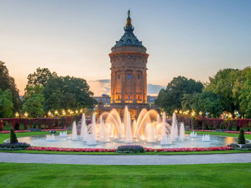 Der Mannheimer Wasserturm in der Dämmerung, davor die beleuchteten Wasserspiele
