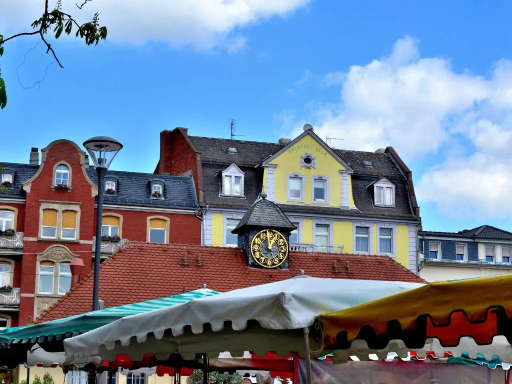 Colourful house facades on the Wilhelmsplatz with the clock, the market awnings below