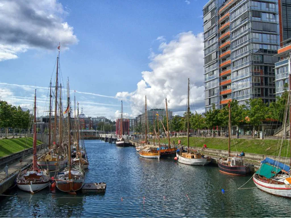 A traditional sailing ship in the harbour basin, a residential tower behind it