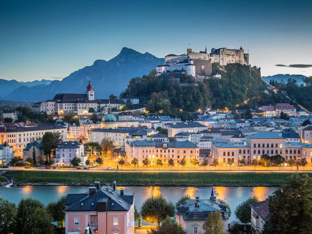 Salzburg at dusk with the lit old town, the Salzach and the fortress above the city