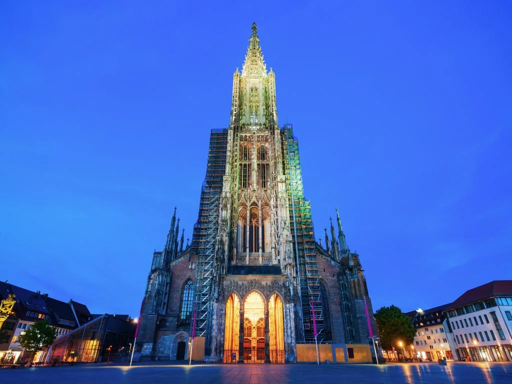 Das Ulmer Münster bei Nacht angestrahlt, der höchste Kirchturm der Welt vor blauem Himmel