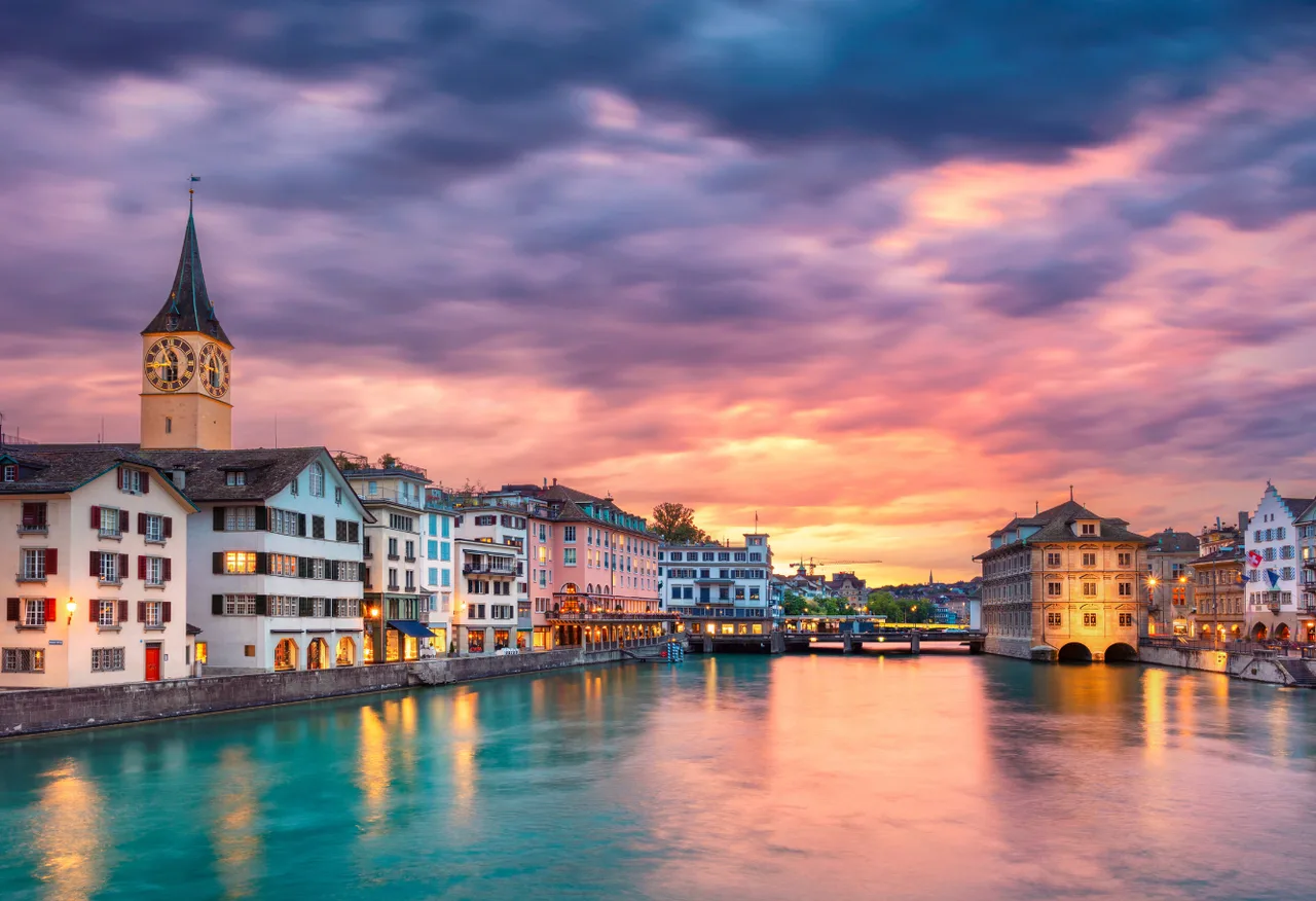 Die Limmat bei Sonnenuntergang mit dem Turm der St.-Peter-Kirche und den Häusern am Quai