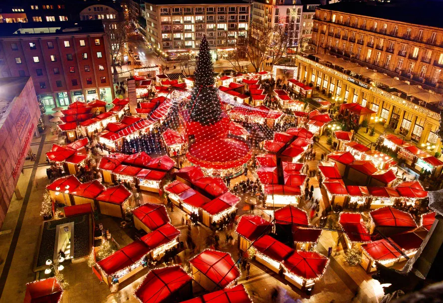 The Christmas market at the cathedral from above, red stall roofs around the lit tree