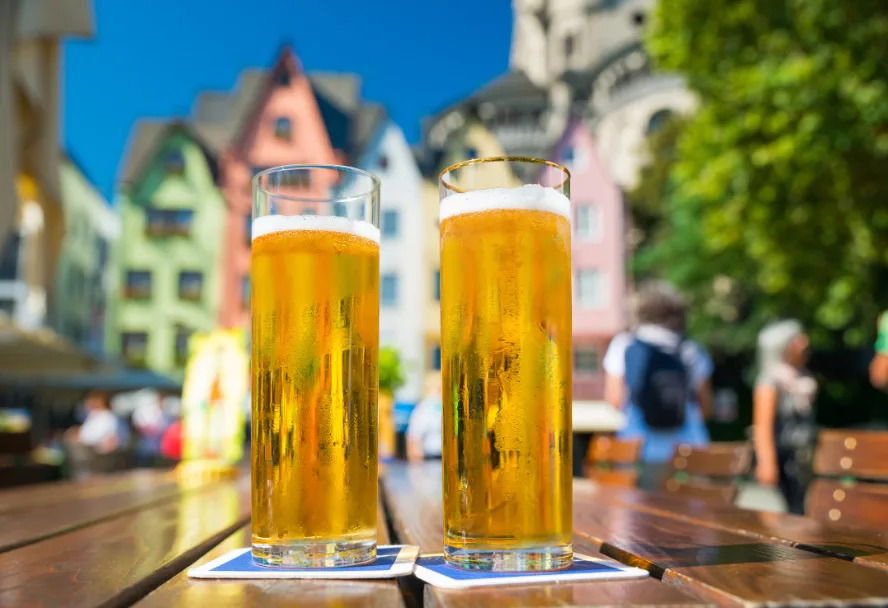 Two Kölsch glasses on a beer garden table in front of the coloured houses at the Fischmarkt