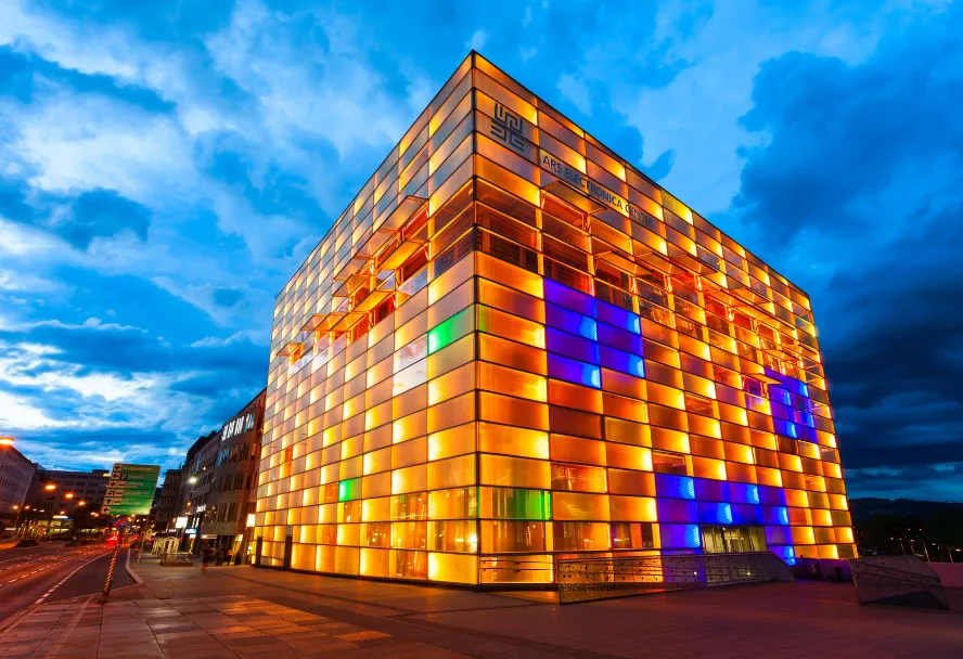 The Ars Electronica Center on the Danube, its glass facade lit orange and blue at night
