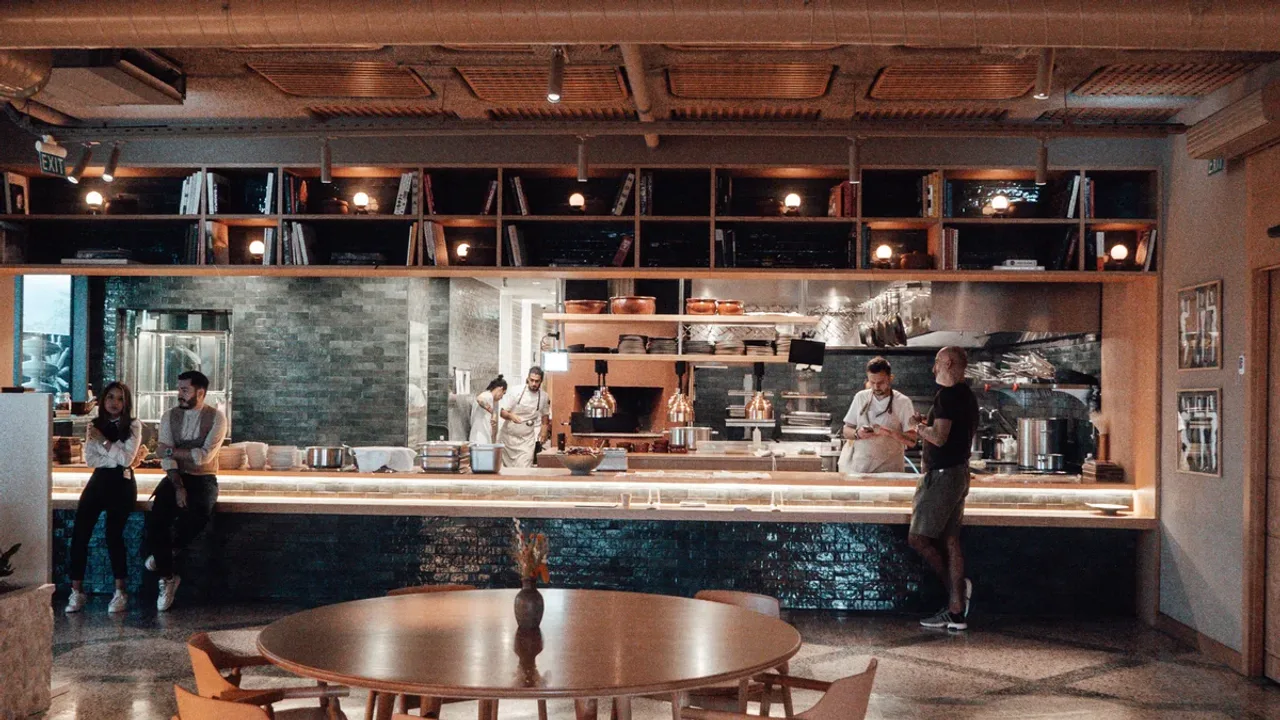 An open kitchen behind a long counter, in front of it a round table with wooden chairs