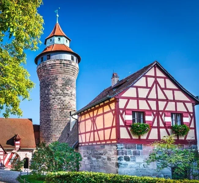 The round Sinwell tower of the Kaiserburg beside a red and white timbered house