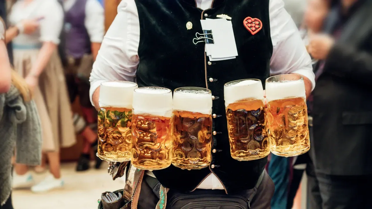 Ein Kellner in Tracht trägt fünf gefüllte Maßkrüge in beiden Händen durch ein Festzelt