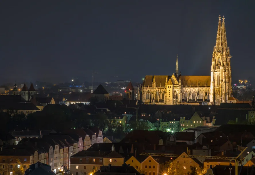 Der beleuchtete Dom St. Peter bei Nacht über den dunklen Dächern der Altstadt