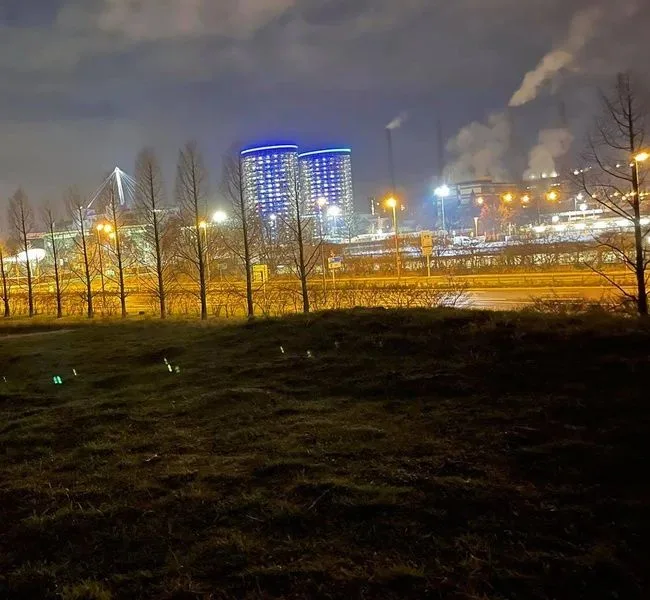 Die blau beleuchteten Rundtürme der Autostadt bei Nacht, dahinter die Schlote des Werks