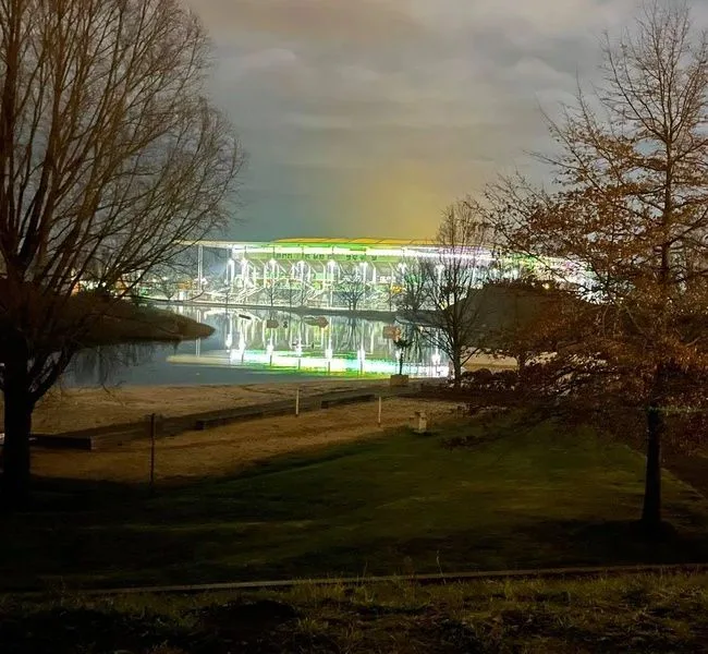 Ein beleuchteter Glasbau am Wasser bei Nacht, sein Licht spiegelt sich im Kanal
