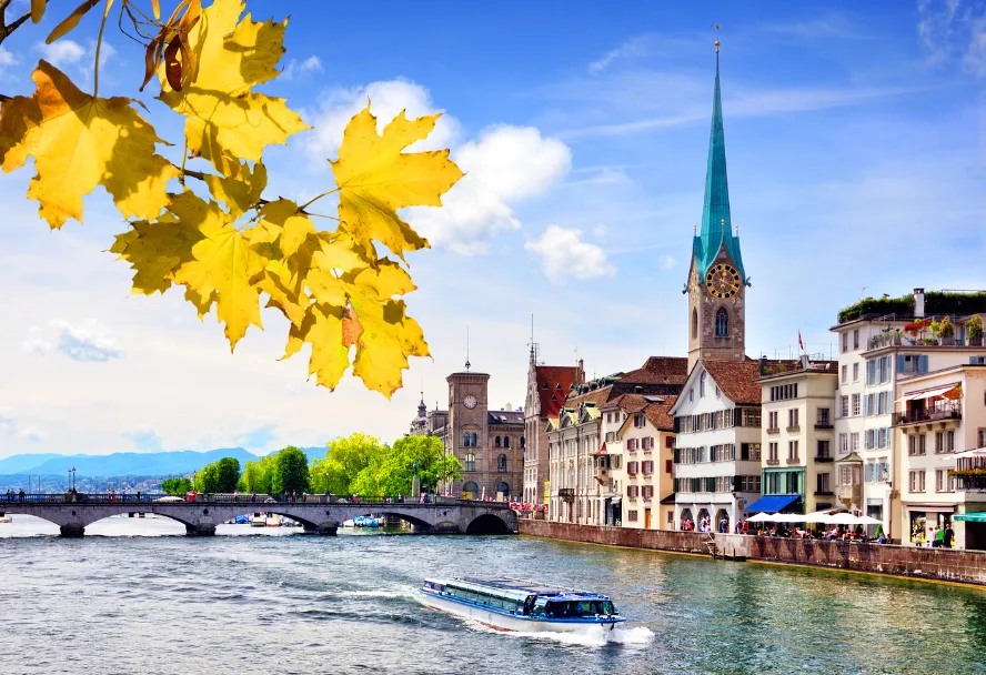 Die Limmat mit dem Turm des Fraumünsters, einem Kursschiff und Herbstlaub im Vordergrund