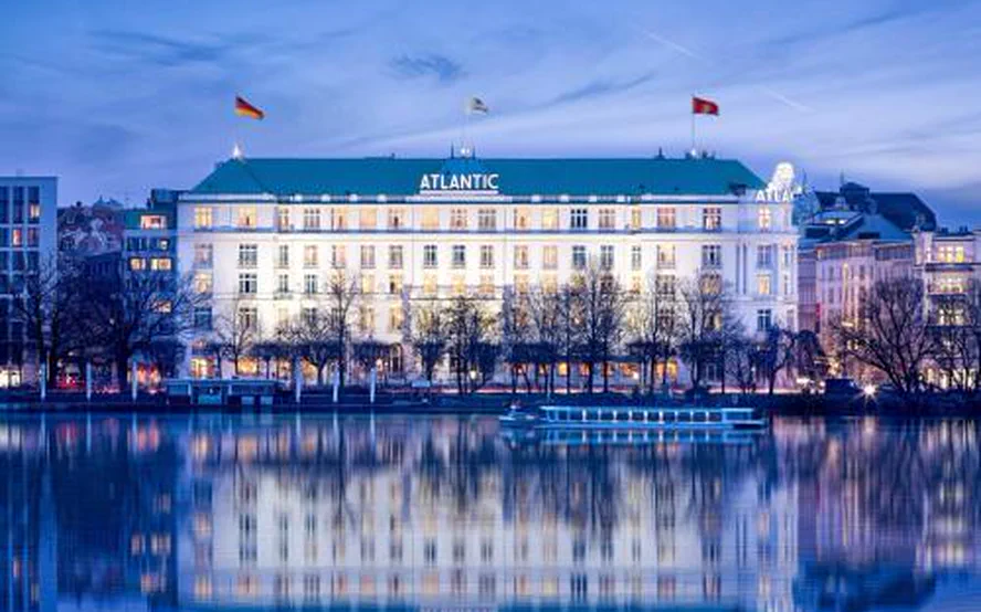 The white building with the ATLANTIC lettering on its roof, mirrored in the Außenalster at blue hour