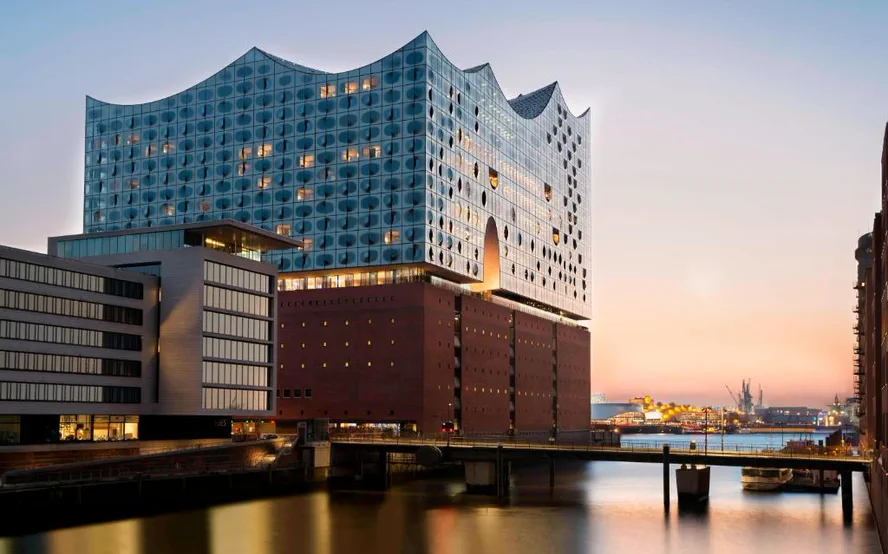 The Elbphilharmonie at dusk above its brick base, the water of the Kaiserhöft in front of it