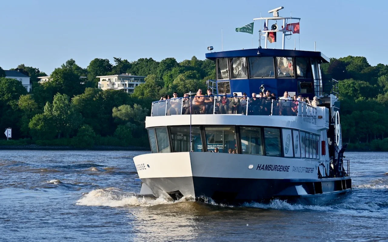 An HVV ferry on the Elbe in front of the green bank at Övelgönne