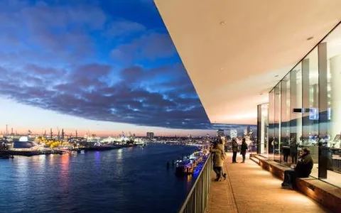 The Plaza terrace of the Elbphilharmonie at blue hour, visitors at the railing above the harbour