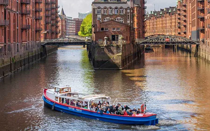 A red launch on the canal by the Wasserschloss, brick warehouses and two bridges all around